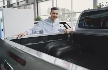 Homem analisando o protetor de caçamba de uma pick-up em concessionária, destacando a importância da proteção para durabilidade.
